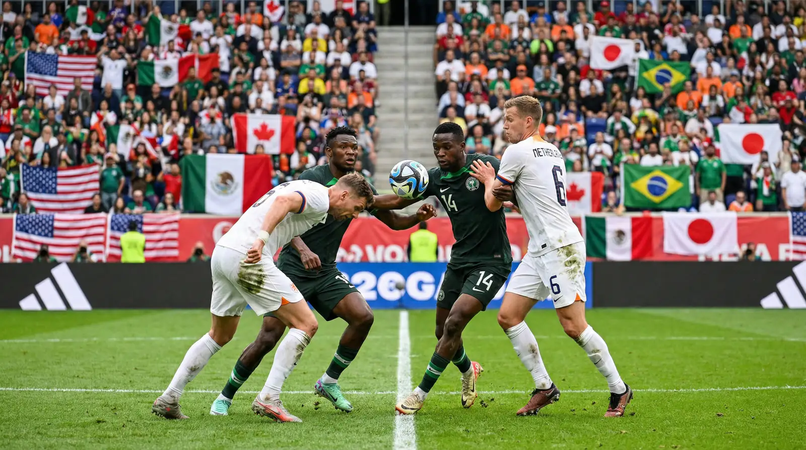 Intenst gruppespil ved VM 2026 med spillere i kamp om bolden på en grøn bane med nationale flag på tribunerne
